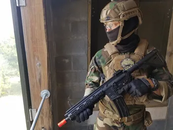 Man in airsoft gear standing in doorway holding a Heckler & Koch airsoft rifle